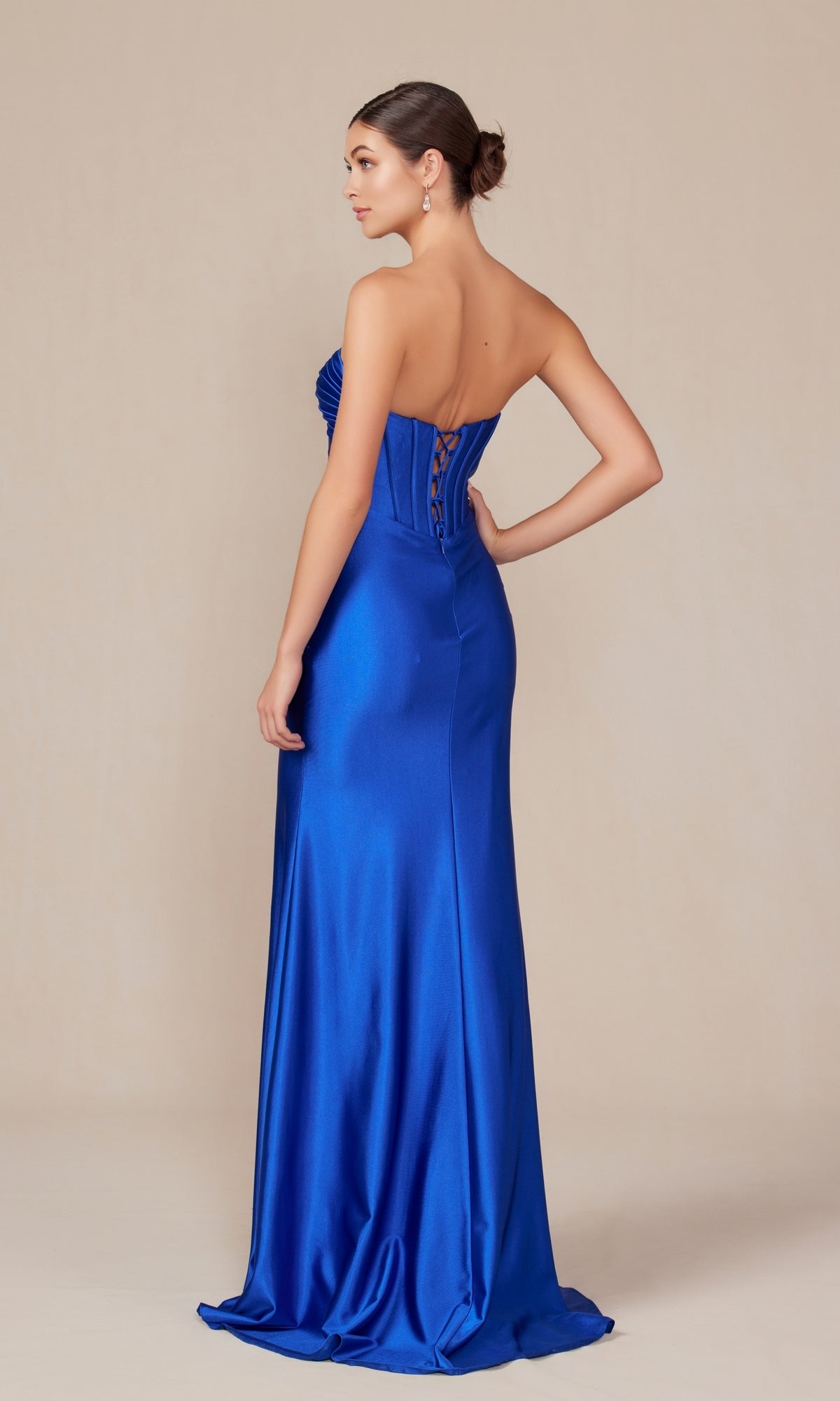 A woman poses in a studio wearing the Nox Anabel T1500, a strapless royal blue satin prom dress featuring a corset-style bodice and elegant lace-up back, with a floor-length sweetheart neckline design.